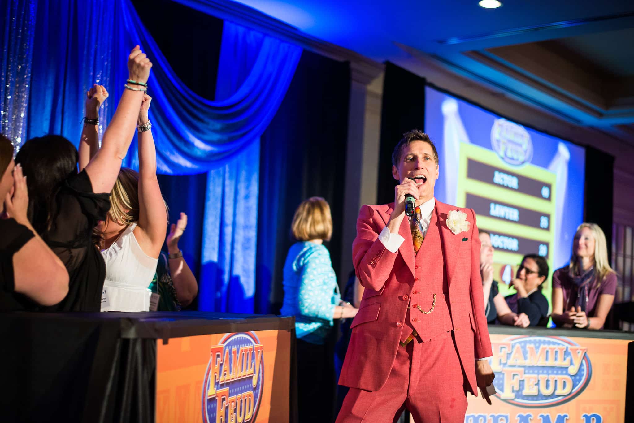 Family Friendly Feud players cheering with fists in the air as the host calls the answer at a corporate event