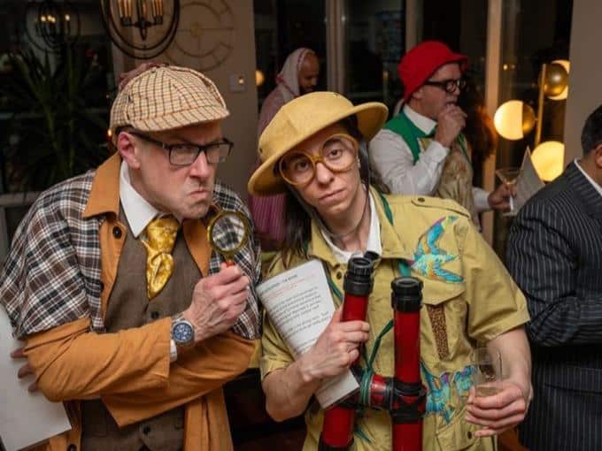 Sheerluck Holmes and a costumed suspect in character at an Engagement Unlimited Murder YOU Mystery, guests behind them