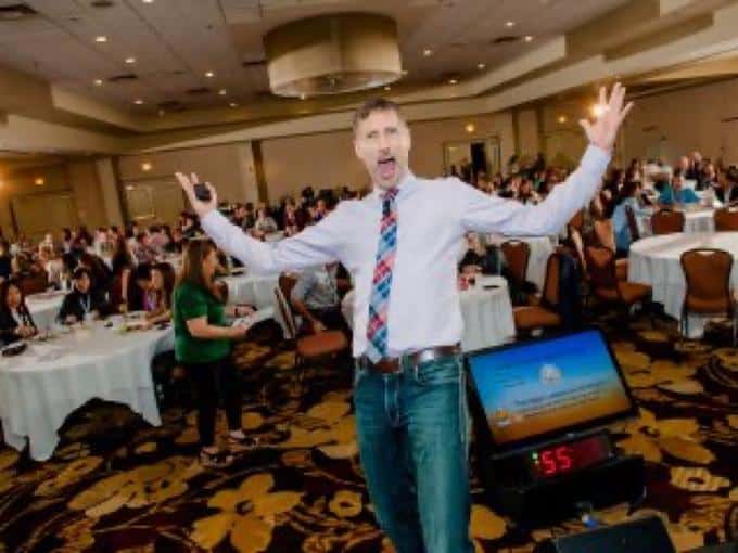 Roger Haskett keynote, arms wide, engaged ballroom