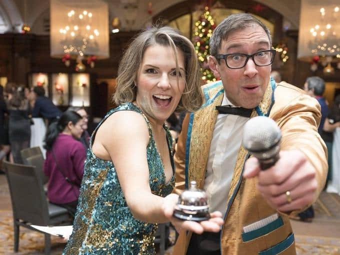 Prize Patrol hosts Stefano and Ella heading for a table with the microphone out at a corporate holiday party