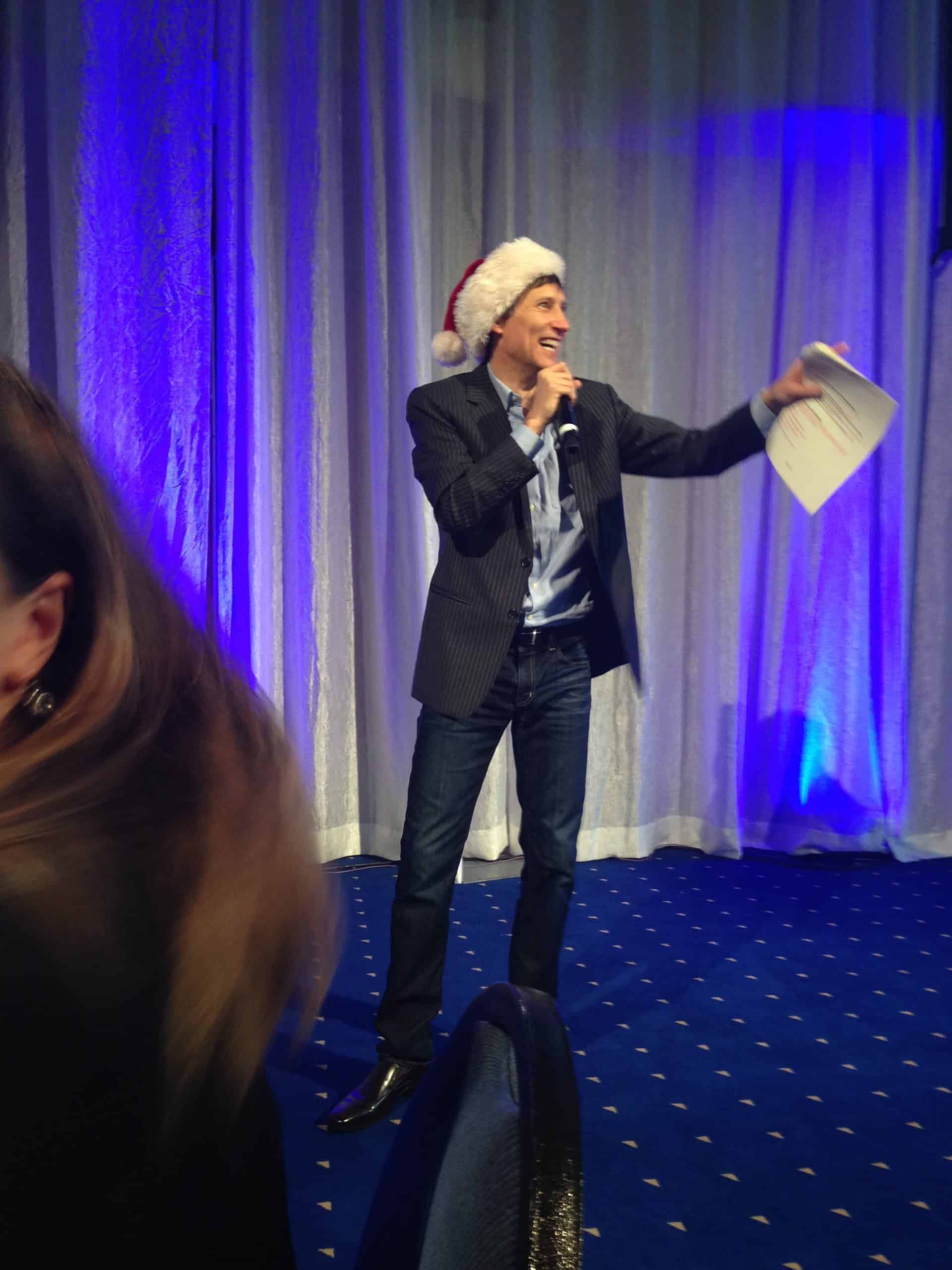 Roger, in a Santa hat, hosts a lively round of holiday trivia at a corporate party.