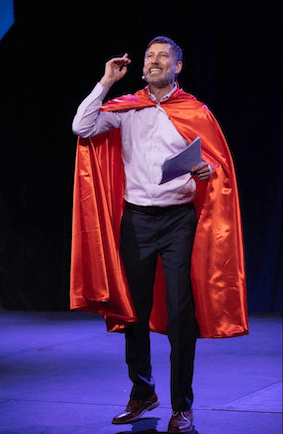 Roger performs a caped entrance while speaking in 2019