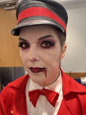 A vampire bellhop character greets guests at a Halloween event