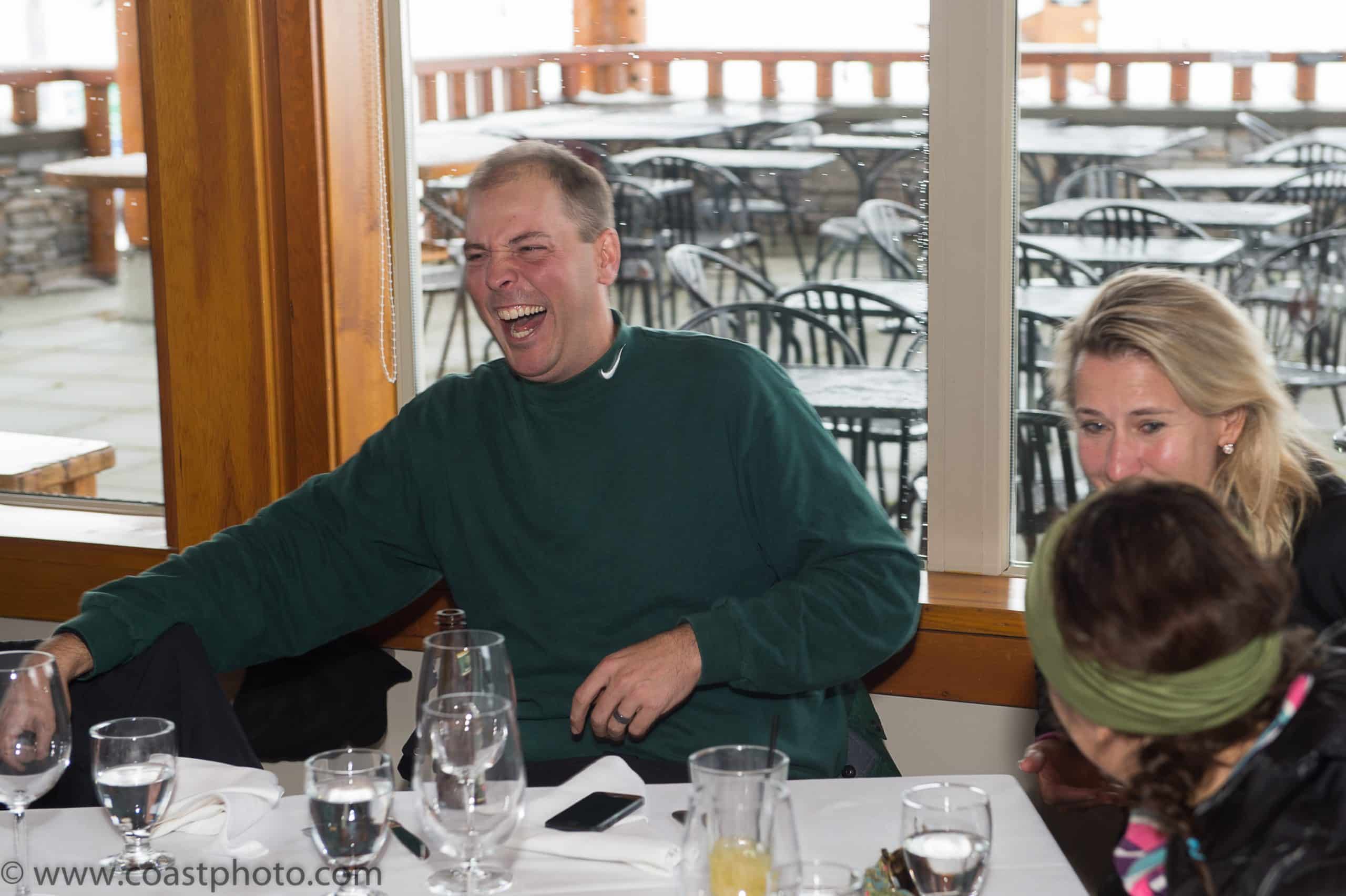 The table breaks into laughter as the reveal lands — the person they'd been talking to all trip was never who he said he was.