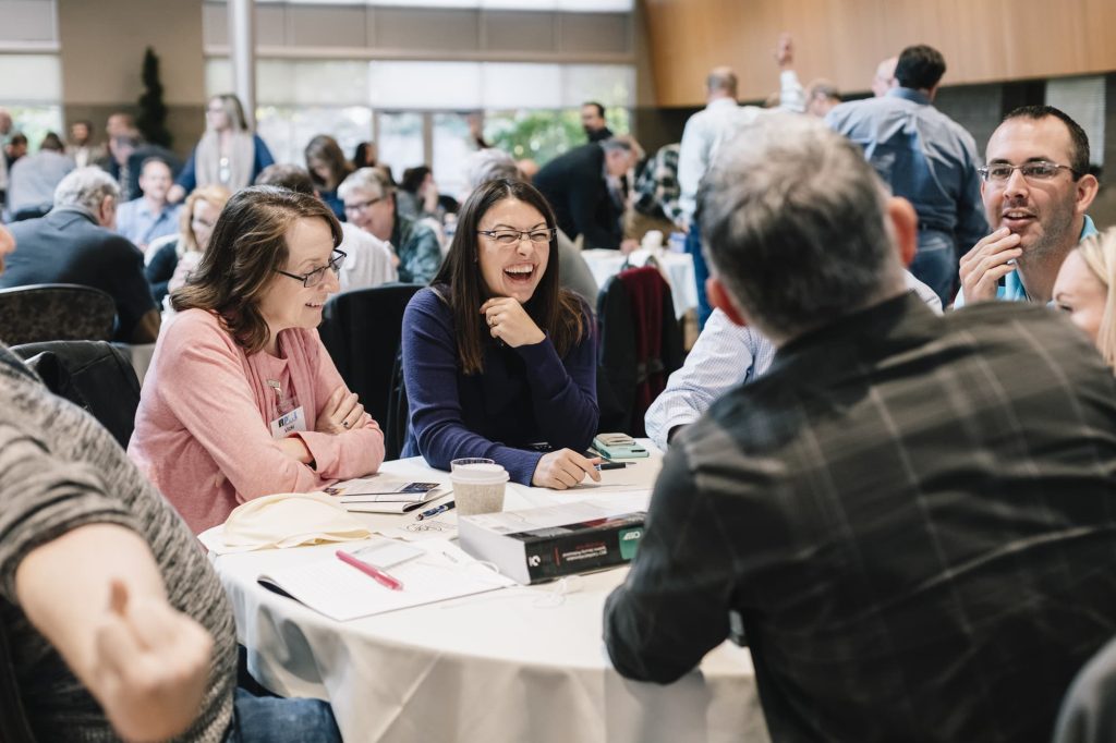 Conference participants laughing together at a round table during an Engagement Unlimited professional development session